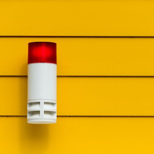 Sirène d'alarme rouge installée sur un mur jaune.
