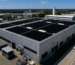 Panneaux photovoltaïques installés sur la toiture d'une entreprise. La toiture est plate et les panneaux photovoltaïques y sont posés. On aperçoit également d'autres usines aux alentours.