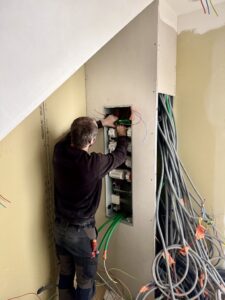 Antoine de la société QR ENERGIES, électricien qualifié et expert en pose de tableaux électriques, en train de passer les câbles et les gaines électriques dans le nouveau tableau électrique installé dans une maison en rénovation à Montélimar. On voit de nombreuses gaines en attente, des gaines télécom, des gaines d'électricité et des murs en placo brut.